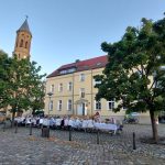 Langer, weiß gedeckter Tisch mit weiß gekleideten Menschen vor einem Gebäude-
