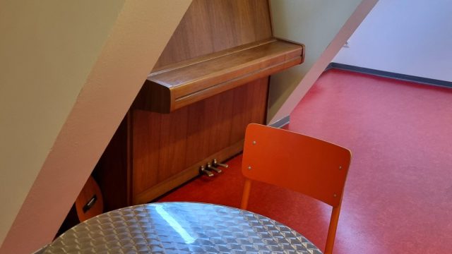 In einem Dachraum stehen ein Klavier und ein Tisch mit Stühlen