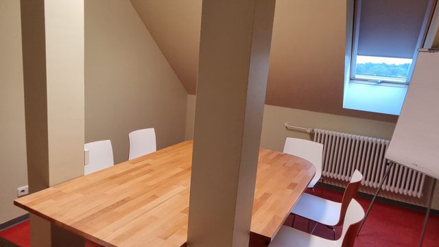 Um einen Tisch in einem Dachraum sind Stühle aufgereiht