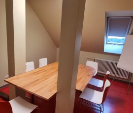 Um einen Tisch in einem Dachraum sind Stühle aufgereiht